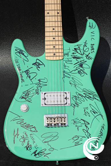 4.	Gitaar close-up  Eén van de twee unieke gitaren die onder de hamer gaan tijdens Rocking Thals 2025. Dit exemplaar werd gesigneerd door internationale topbands op Graspop Metal Meeting. De rode gitaar is dan weer gesigneerd door niemand minder dan AVATAR op Alcatraz.